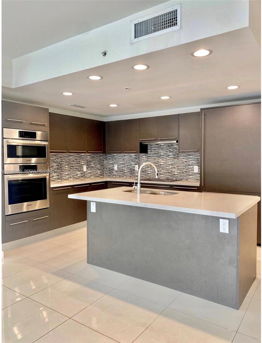 A modern kitchen features dark cabinetry, a central island with a sink, and stainless appliances — 7661 NW 107th Ave # 407, Doral FL 33178, DORAL, FL