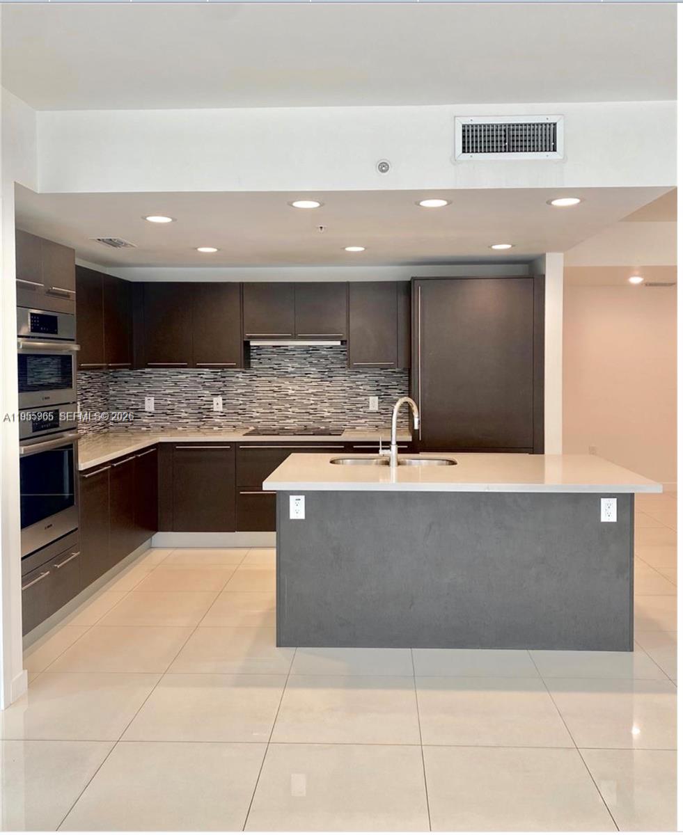 A modern kitchen features dark cabinetry, a central island with a sink, and tile flooring — 7661 NW 107th Ave # 407, Doral FL 33178, DORAL, FL