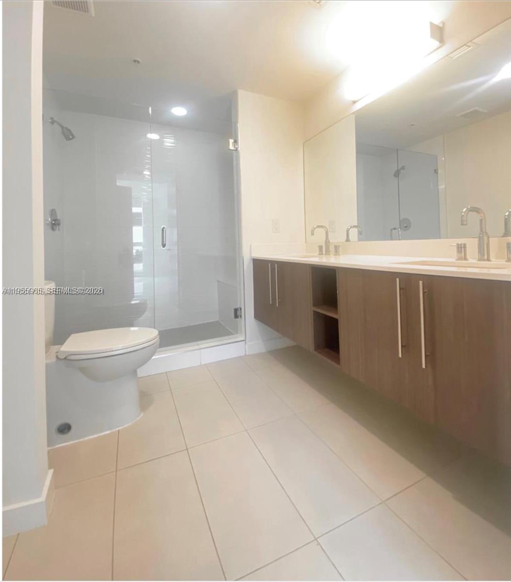 A modern bathroom features a floating wood vanity, a glass-enclosed shower, and tile flooring — 7661 NW 107th Ave # 407, Doral FL 33178, DORAL, FL
