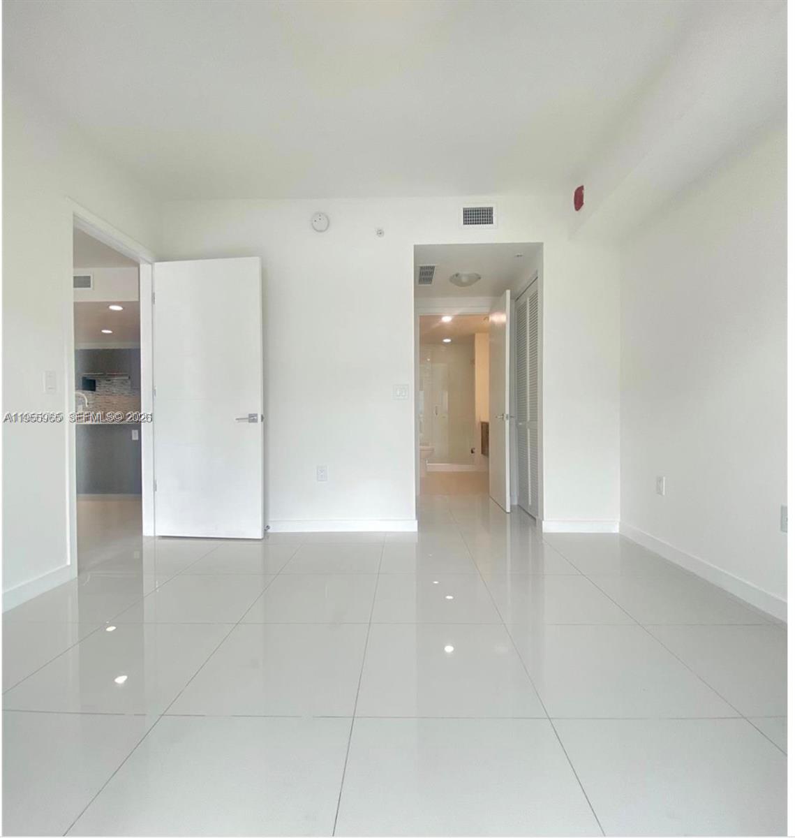 An empty room with white walls and glossy white tile flooring features two doorways — 7661 NW 107th Ave # 407, Doral FL 33178, DORAL, FL