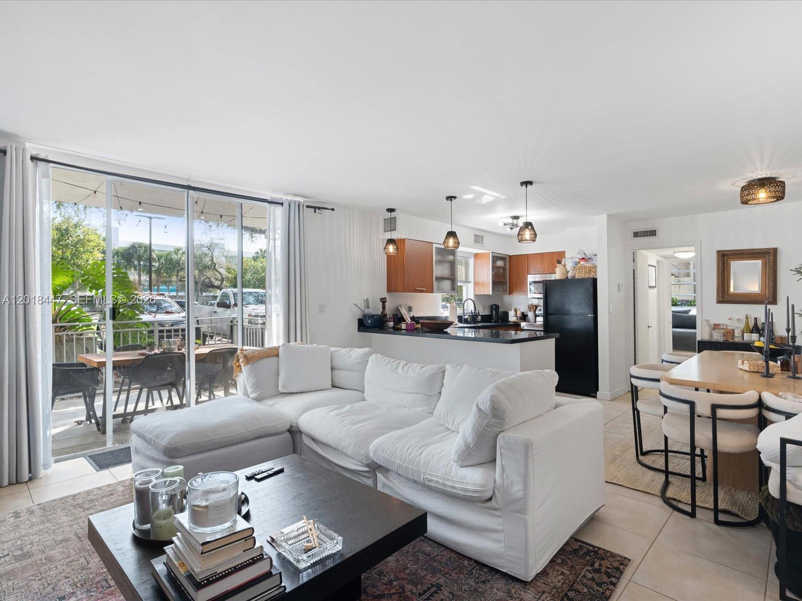 A living room with a white sectional sofa, kitchen, and sliding glass doors to a patio — 680 NE 64th St # A110, Miami FL 33138, MIAMI, FL