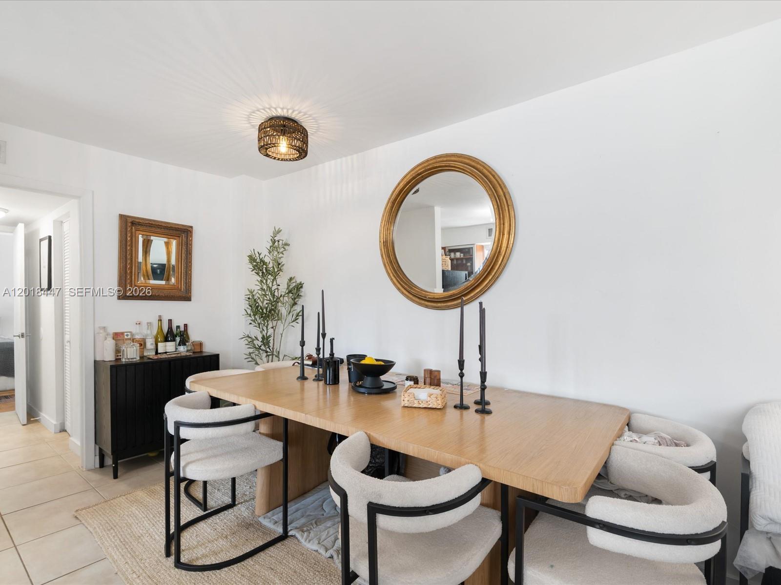 A dining room features a wooden table, cream-colored chairs, a round mirror, and a sideboard — 680 NE 64th St # A110, Miami FL 33138, MIAMI, FL