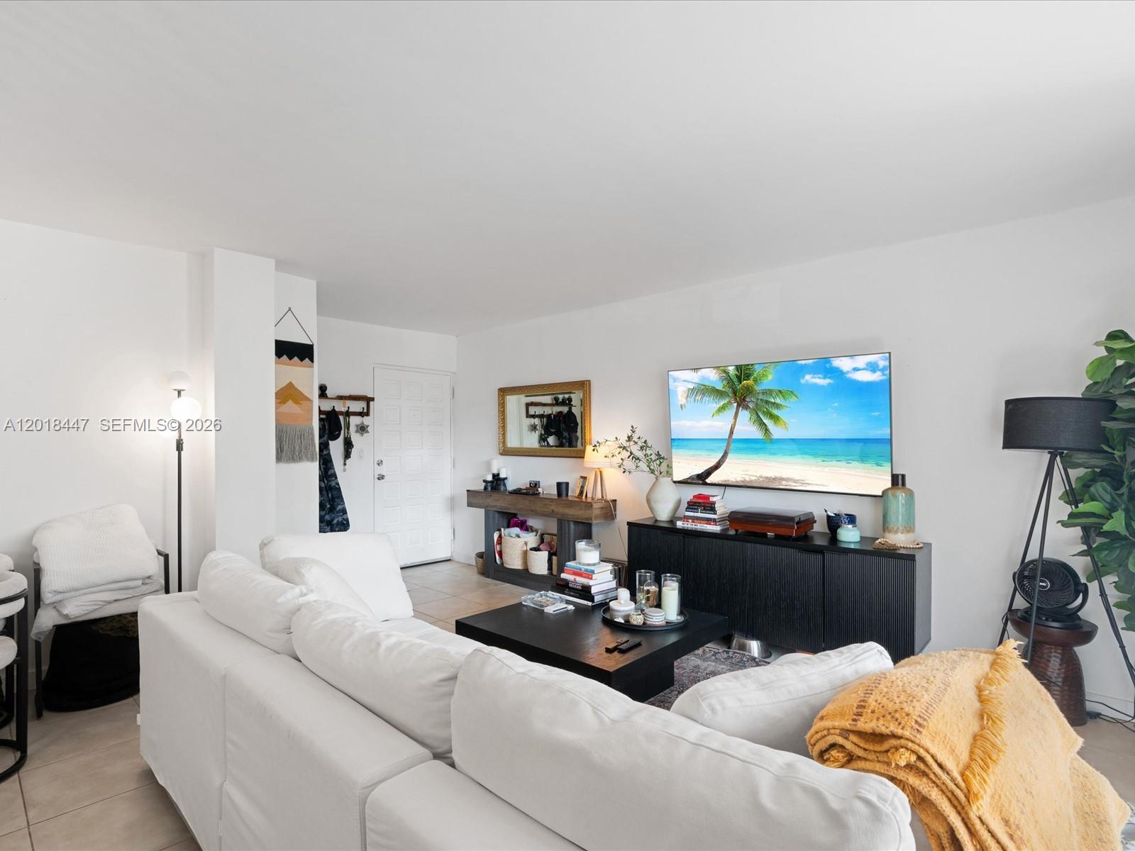 A living room features a white sectional sofa, a black coffee table, and a wall-mounted television — 680 NE 64th St # A110, Miami FL 33138, MIAMI, FL