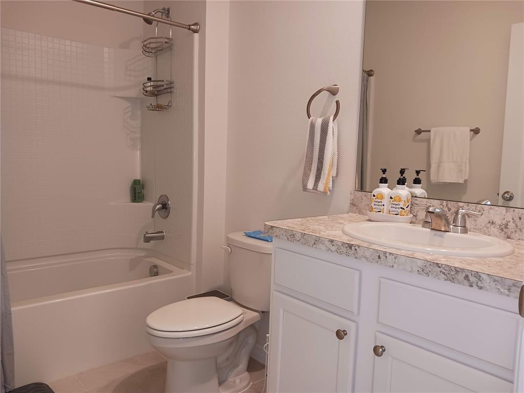 A bathroom features a white vanity with a stone countertop, a toilet, and a tub-shower — 563 HONEY BELL ROAD, WINTER HAVEN, FL