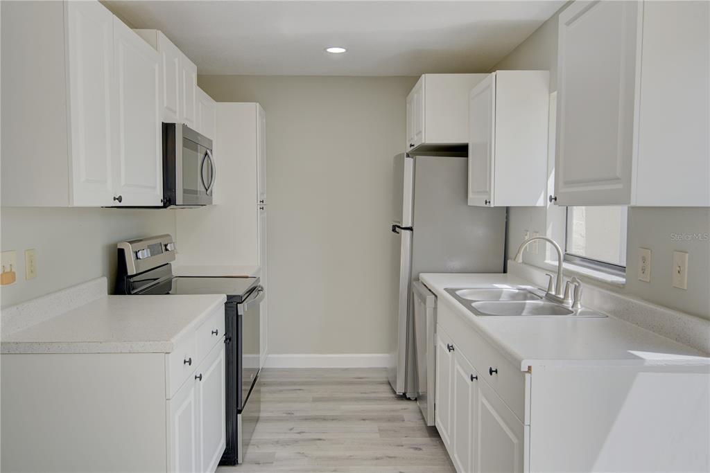 A galley kitchen features white cabinets, stainless steel appliances, and light-colored wood-look flooring — 6296 RIVER RUN PLACE UNIT 194, ORLANDO, FL