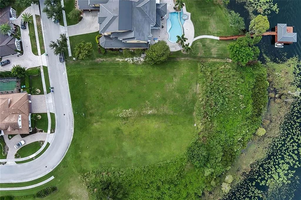 An aerial view shows a vacant grassy lot situated between a residential street and a lake — 5727 EMERINGTON CRESCENT, ORLANDO, FL