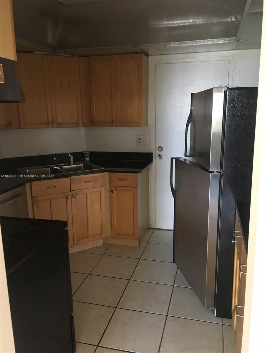 A kitchen features light wood cabinets, black countertops, stainless steel appliances, and tiled flooring — 3301 Spanish Moss Ter # 906, Lauderhill FL 33319, LAUDERHILL, FL