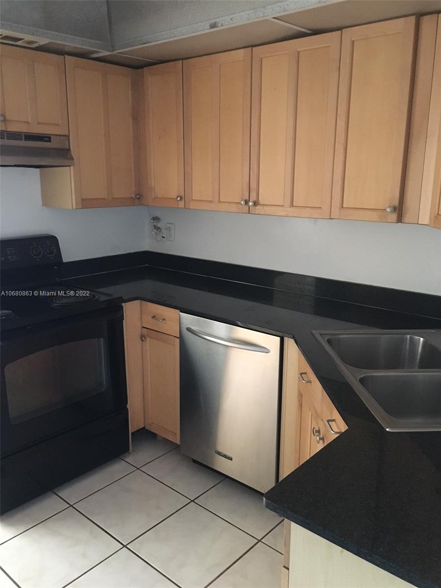 A kitchen features light wood cabinets, black countertops, stainless steel appliances, and white floor tiles — 3301 Spanish Moss Ter # 906, Lauderhill FL 33319, LAUDERHILL, FL