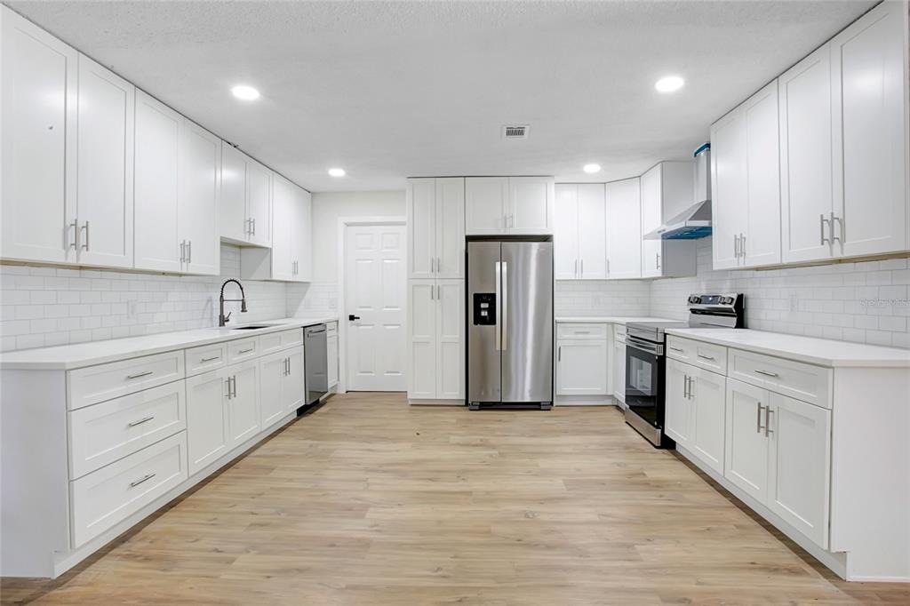 A modern kitchen features white cabinets, stainless steel appliances, white countertops, and light wood flooring — 1221 FOREST CIRCLE, ALTAMONTE SPRINGS, FL