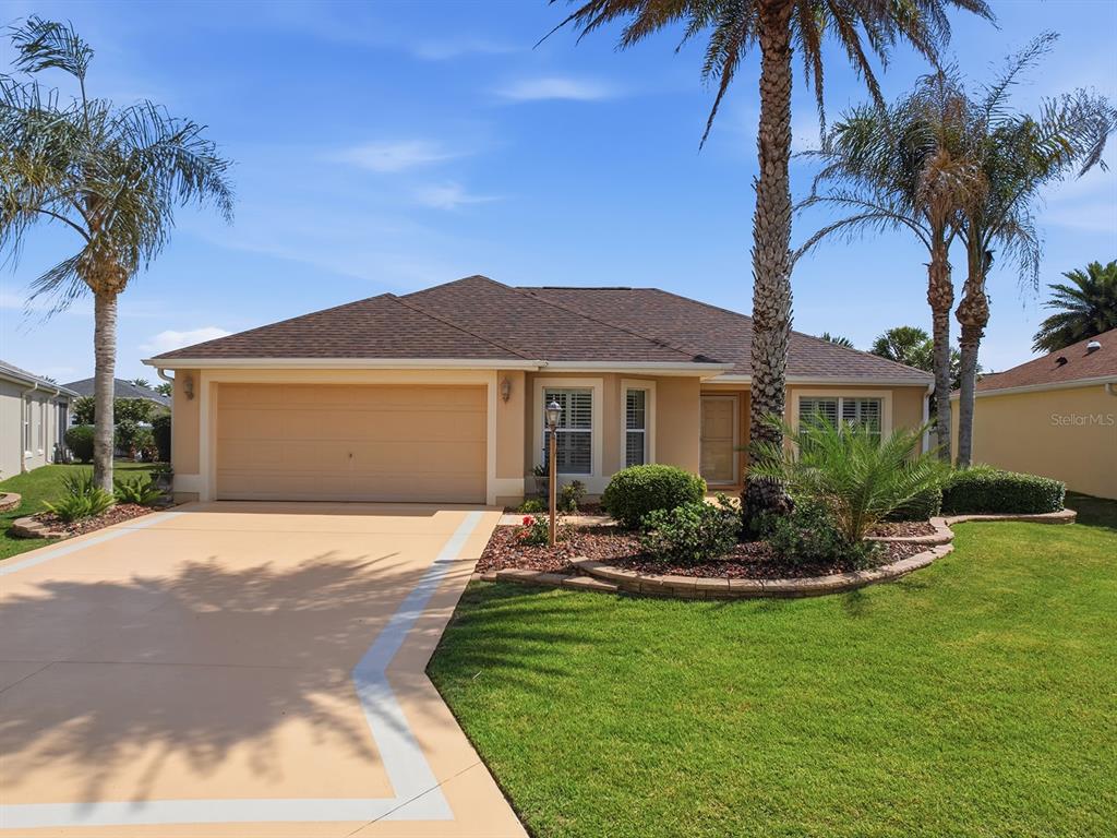 A single-story house with a tan exterior, a two-car garage, and palm trees in front — 1104 ALCOVE LOOP, THE VILLAGES, FL