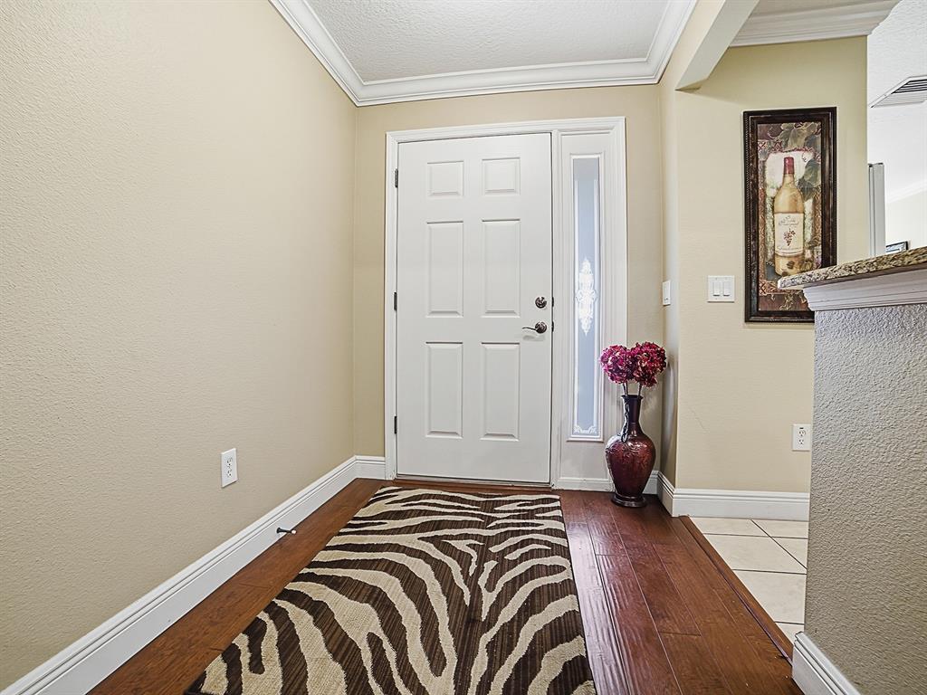 An entryway features a white front door, hardwood flooring, a zebra-print rug, and a vase — 1104 ALCOVE LOOP, THE VILLAGES, FL