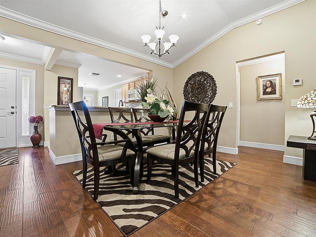 A dining room features a glass-topped table, six chairs, a zebra-print rug, and hardwood floors — 1104 ALCOVE LOOP, THE VILLAGES, FL