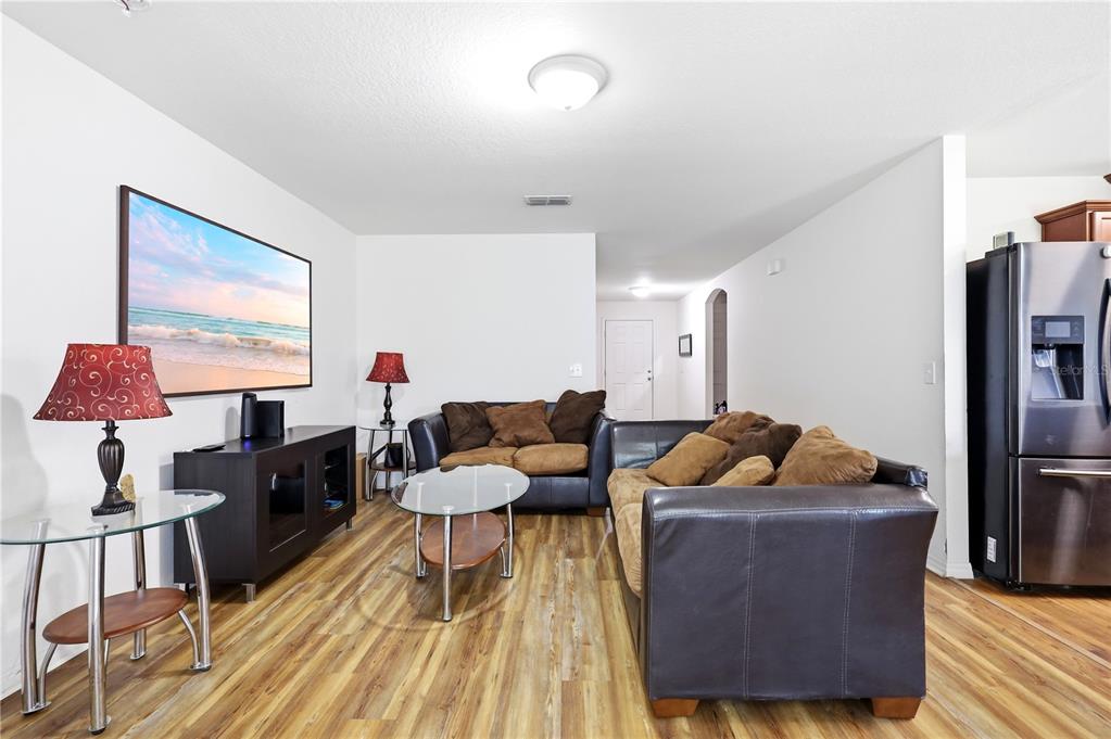 A living room features wood-look flooring, a dark leather sofa, and a wall-mounted television — 184 ELEUTHERA DRIVE, LAKE ALFRED, FL