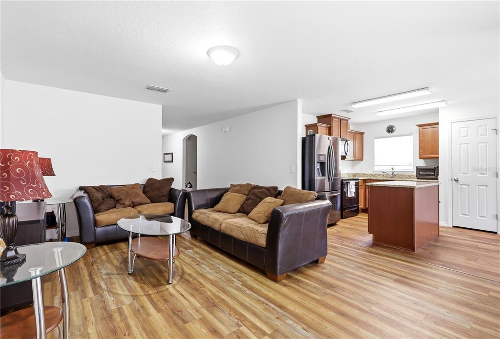 An open-concept living room and kitchen featuring wood-look flooring and brown leather furniture — 184 ELEUTHERA DRIVE, LAKE ALFRED, FL