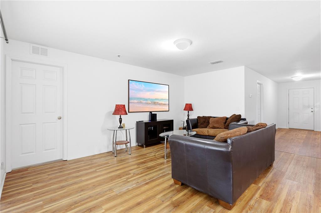 A living room features wood-look flooring, a dark leather sofa, and a wall-mounted television — 184 ELEUTHERA DRIVE, LAKE ALFRED, FL