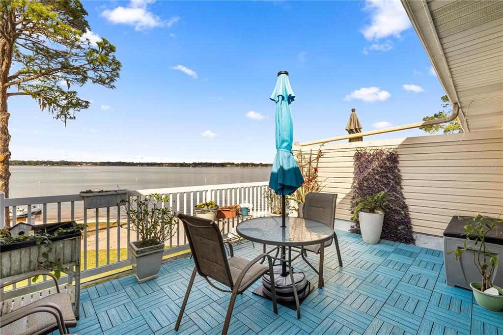 A deck with blue interlocking tiles, a patio table, and a view of the water — 11001 SE SUNSET HARBOR ROAD UNIT B14, SUMMERFIELD, FL