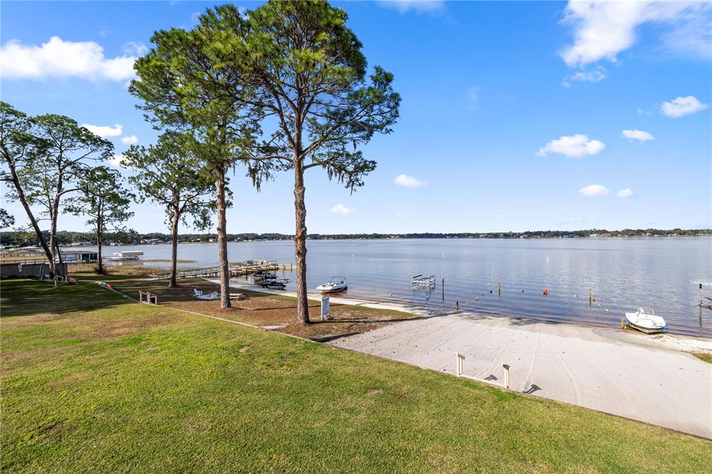 A grassy lawn slopes down to a sandy boat ramp and a lake with docks — 11001 SE SUNSET HARBOR ROAD UNIT B14, SUMMERFIELD, FL