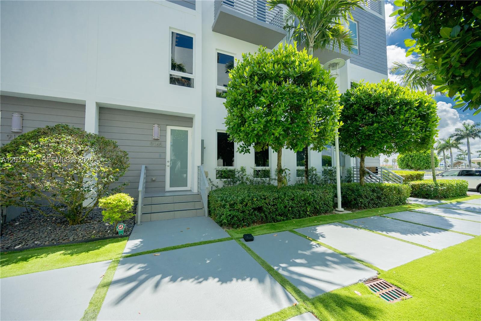 The exterior of a modern multi-story townhouse features a gray door, stairs, and landscaping — 9165 NW 33rd St, Doral FL 33172, DORAL, FL