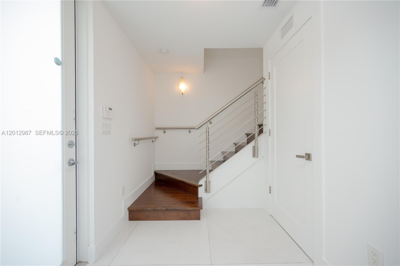 A modern entryway features white tile flooring, a wooden staircase, and a metal railing — 9165 NW 33rd St, Doral FL 33172, DORAL, FL