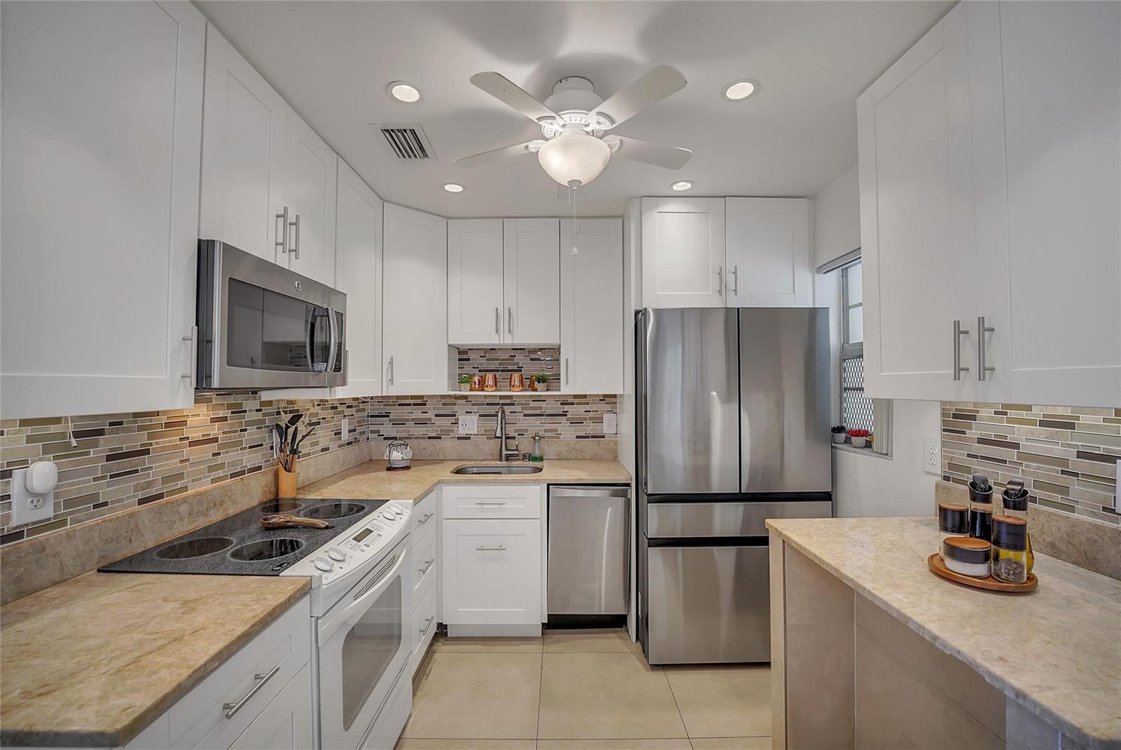 A kitchen features white cabinets, stainless steel appliances, a tiled backsplash, and beige countertops — 700 Layne Boulevard # 301, Hallandale Beach FL 33009, HALLANDALE BEACH, FL