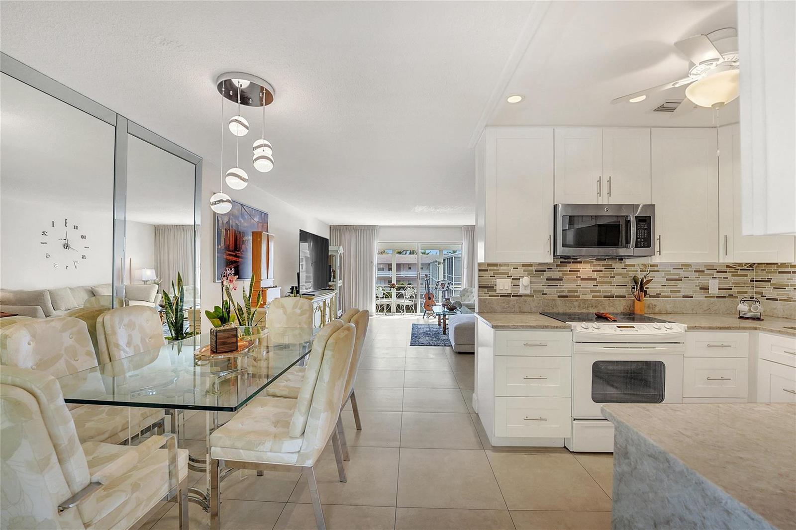A dining area with a glass table and mirrored wall sits adjacent to a white kitchen — 700 Layne Boulevard # 301, Hallandale Beach FL 33009, HALLANDALE BEACH, FL