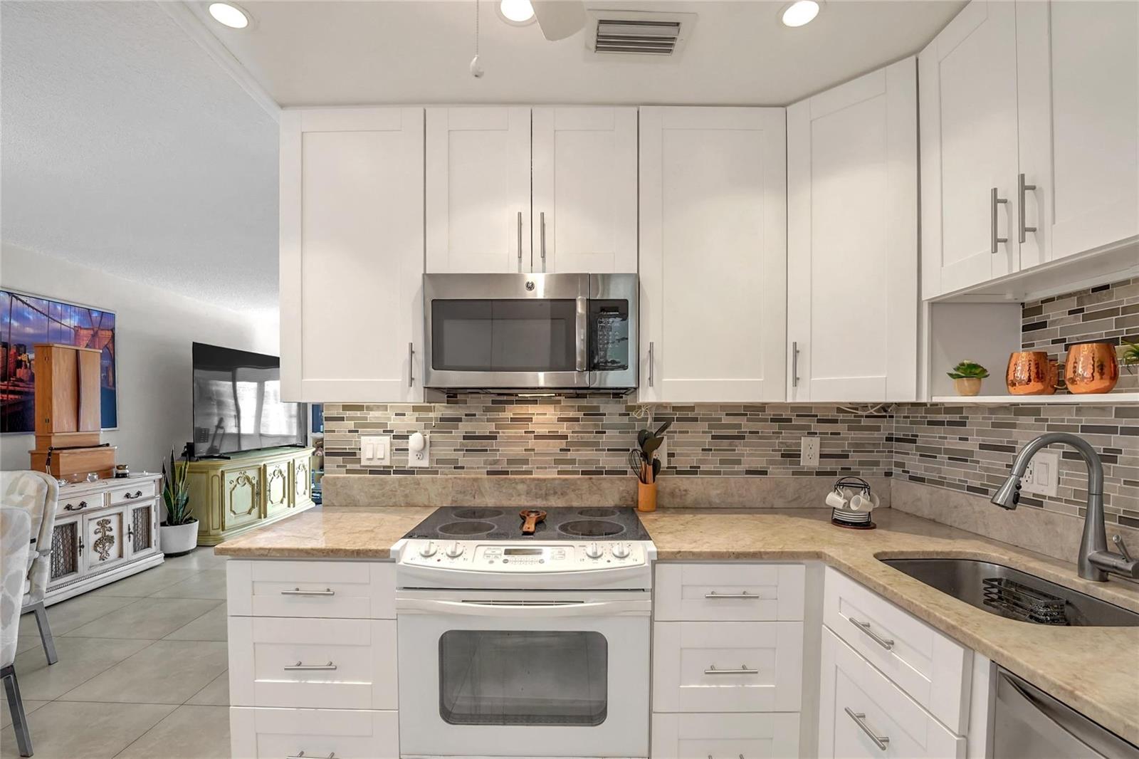 A kitchen features white cabinets, stainless steel appliances, a stone countertop, and a tiled backsplash — 700 Layne Boulevard # 301, Hallandale Beach FL 33009, HALLANDALE BEACH, FL