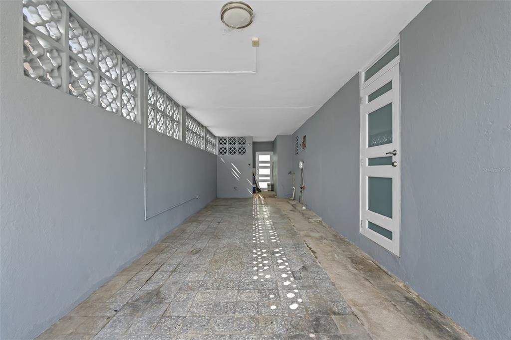 A long, narrow covered carport features gray walls, a tiled floor, and decorative breeze blocks — 1210 CALLE MARIA BUSTAMANTE, SAN JUAN, PR