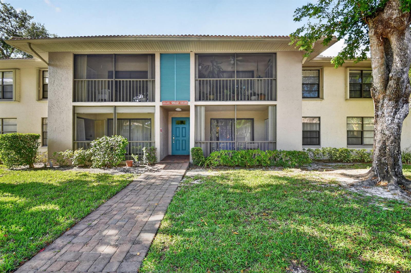 A two-story apartment building features a brick walkway leading to a central blue front door — 9810 Pineapple Tree Drive # 103, Boynton Beach FL 33436, BOYNTON BEACH, FL