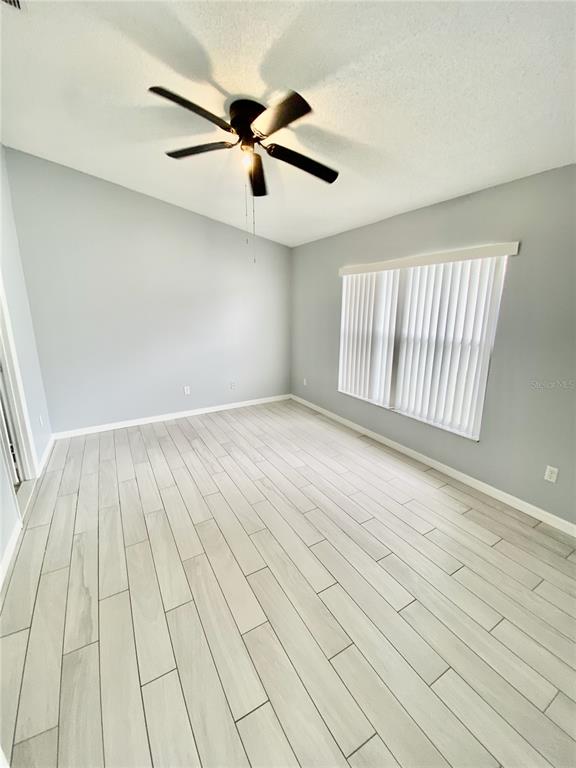 An empty room features light gray walls, wood-look tile flooring, a ceiling fan, and vertical blinds — 2298 SANTA LUCIA STREET, KISSIMMEE, FL
