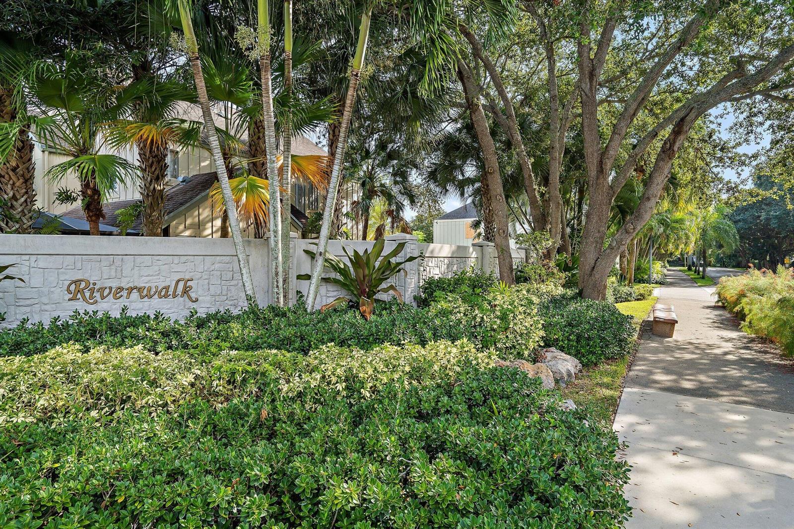 A stone wall with the word Riverwalk sits behind lush landscaping and a paved walkway — 6343 Riverwalk Lane # 3, Jupiter FL 33458, JUPITER, FL