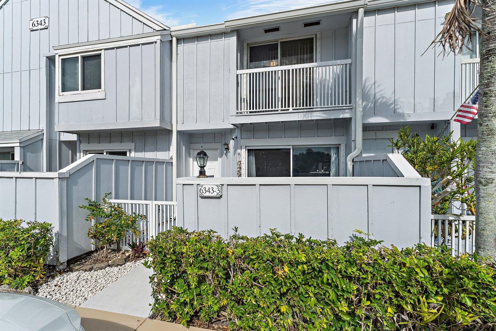 The exterior of a two-story gray townhouse features a balcony and a fenced patio area — 6343 Riverwalk Lane # 3, Jupiter FL 33458, JUPITER, FL