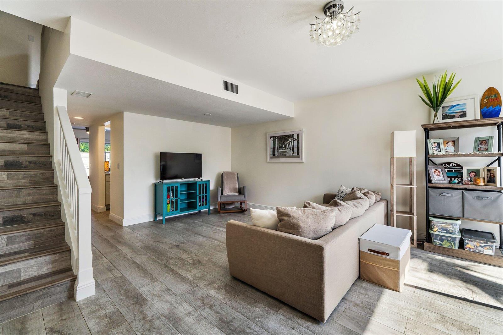 A living room features wood-look tile flooring, a beige sofa, a teal media console, and stairs — 6343 Riverwalk Lane # 3, Jupiter FL 33458, JUPITER, FL