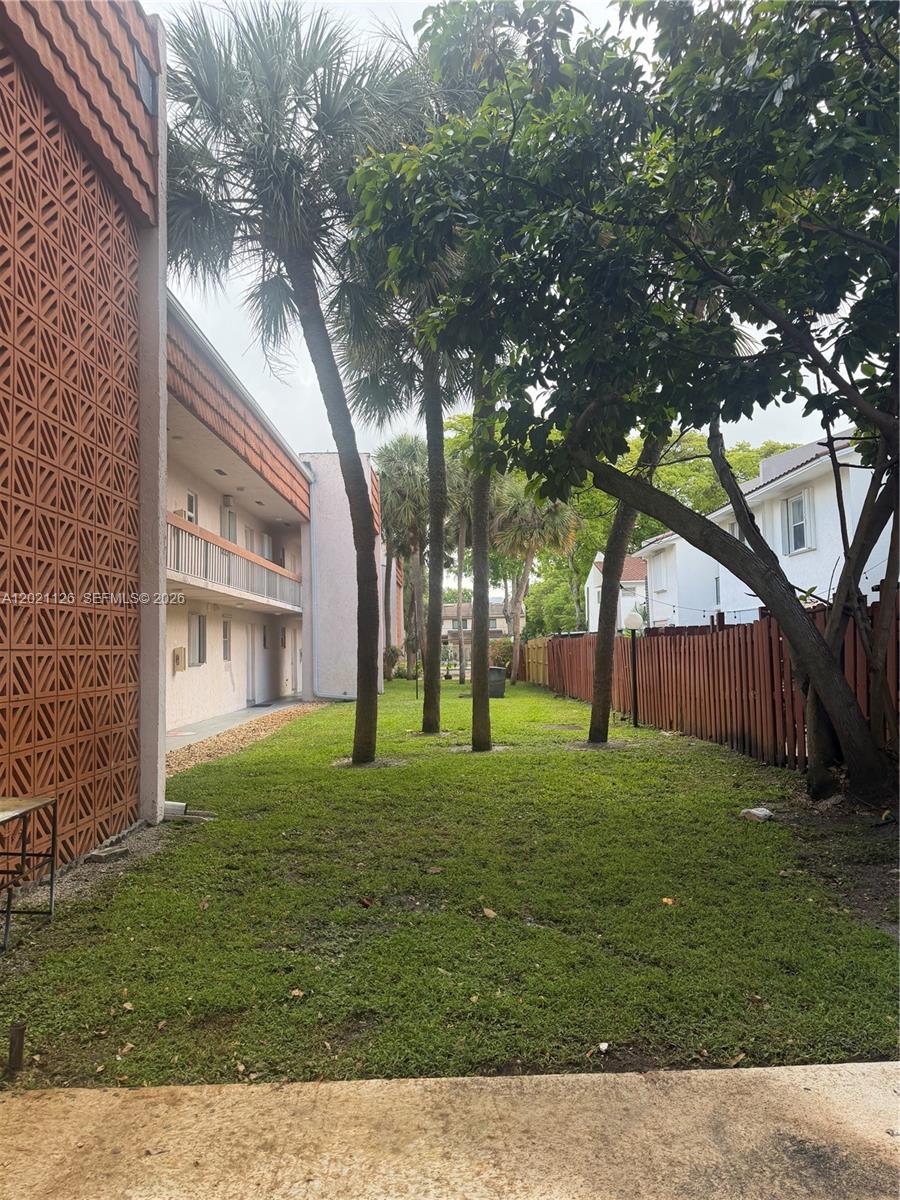 A grassy courtyard sits between a multi-story apartment building and a wooden privacy fence — 7610 Stirling Rd # 205G, Davie FL 33024, DAVIE, FL