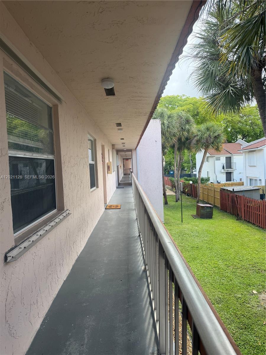 An exterior walkway with a metal railing overlooks a grassy yard with palm trees — 7610 Stirling Rd # 205G, Davie FL 33024, DAVIE, FL