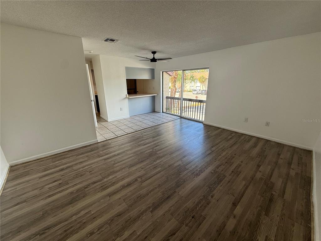 An open living room with wood-look flooring, a ceiling fan, and a sliding glass door — 2636 HIDDEN LAKE DRIVE N UNIT H, SARASOTA, FL