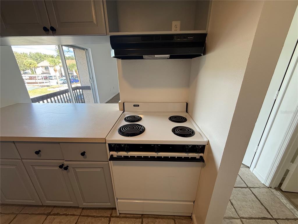 A kitchen features a white electric stove, a range hood, and gray cabinets — 2636 HIDDEN LAKE DRIVE N UNIT H, SARASOTA, FL