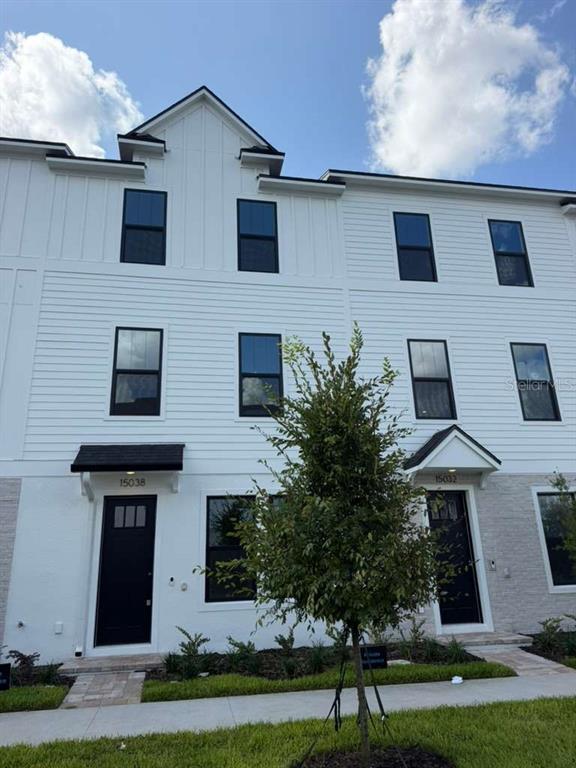 A three-story white townhouse exterior with black window frames and two front entry doors — 15038 GROVESIDE ROAD, WINTER GARDEN, FL