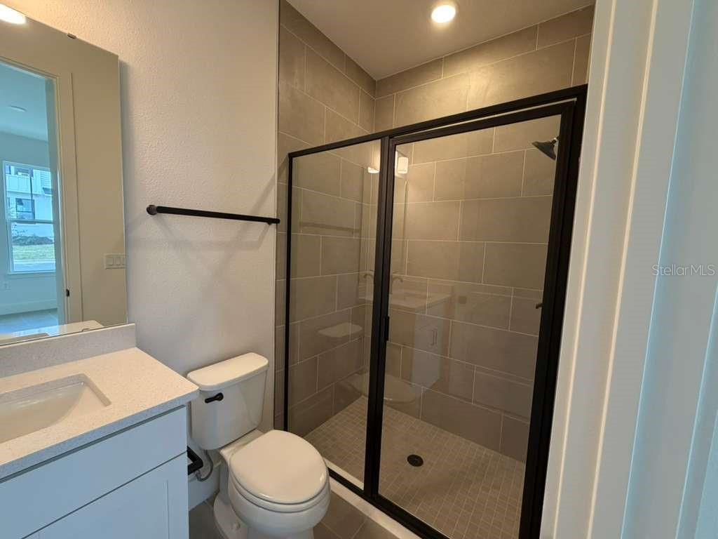 A bathroom features a white vanity, a toilet, and a glass-enclosed shower with tiled walls — 15038 GROVESIDE ROAD, WINTER GARDEN, FL