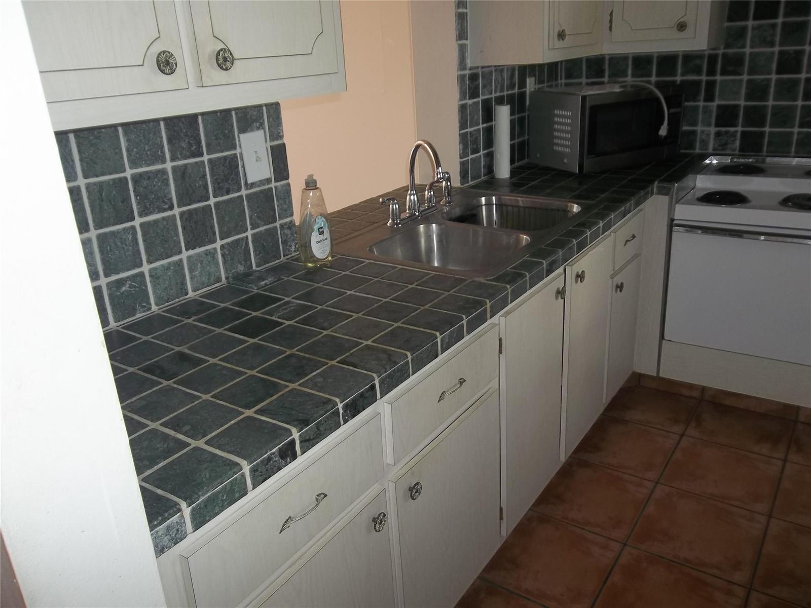 A kitchen features white cabinets, a dark tiled countertop, a double sink, and tiled flooring — 1893 S Ocean Drive # 302, Hallandale Beach FL 33009, HALLANDALE BEACH, FL