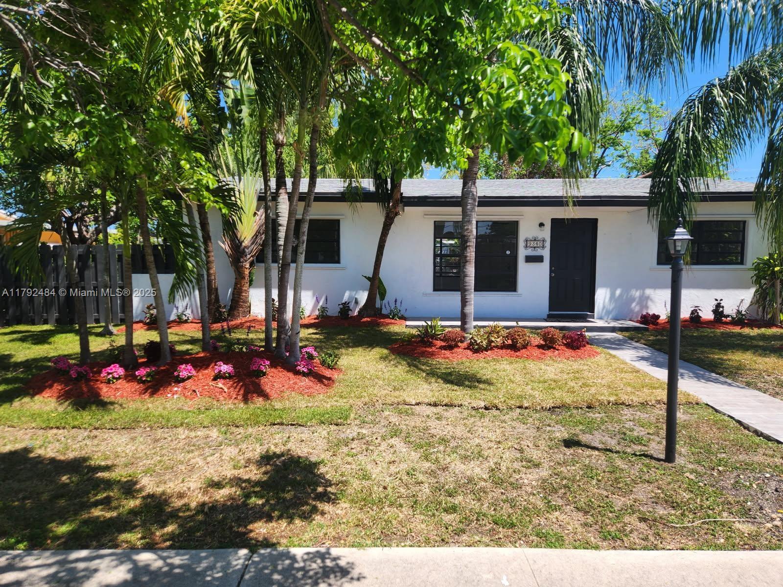A white single-story house features a dark front door, palm trees, and red mulch landscaping — 9340 Martinique Dr, Cutler Bay FL 33189, CUTLER BAY, FL