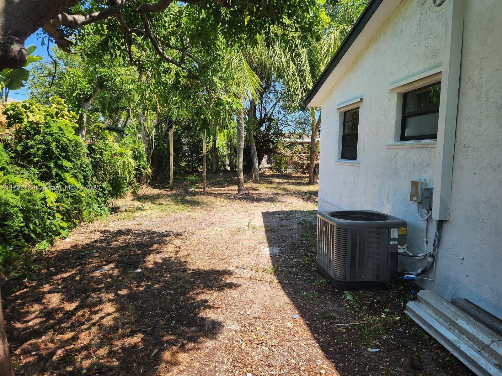 A side yard features a white stucco house wall, an air conditioning unit, and trees — 9340 Martinique Dr, Cutler Bay FL 33189, CUTLER BAY, FL