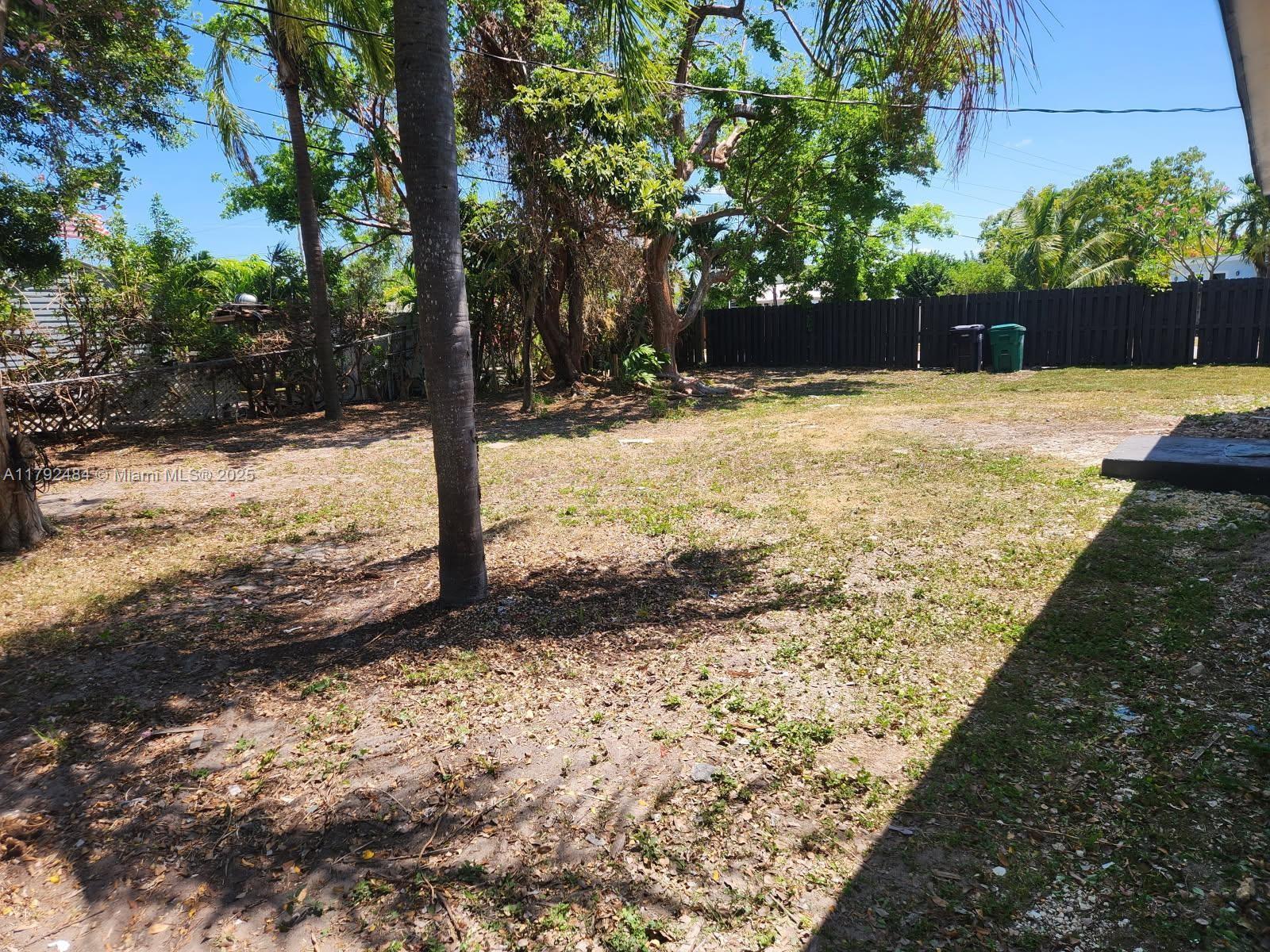 A backyard features a grassy lawn, mature trees, and a dark wooden privacy fence — 9340 Martinique Dr, Cutler Bay FL 33189, CUTLER BAY, FL