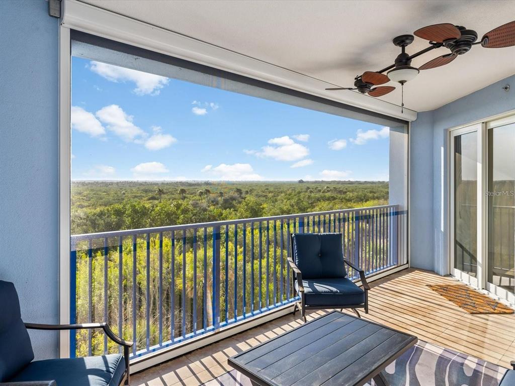 A covered balcony features a ceiling fan, outdoor furniture, and a view of dense trees — 5300 SOUTH ATLANTIC AVENUE UNIT 19406, NEW SMYRNA BEACH, FL