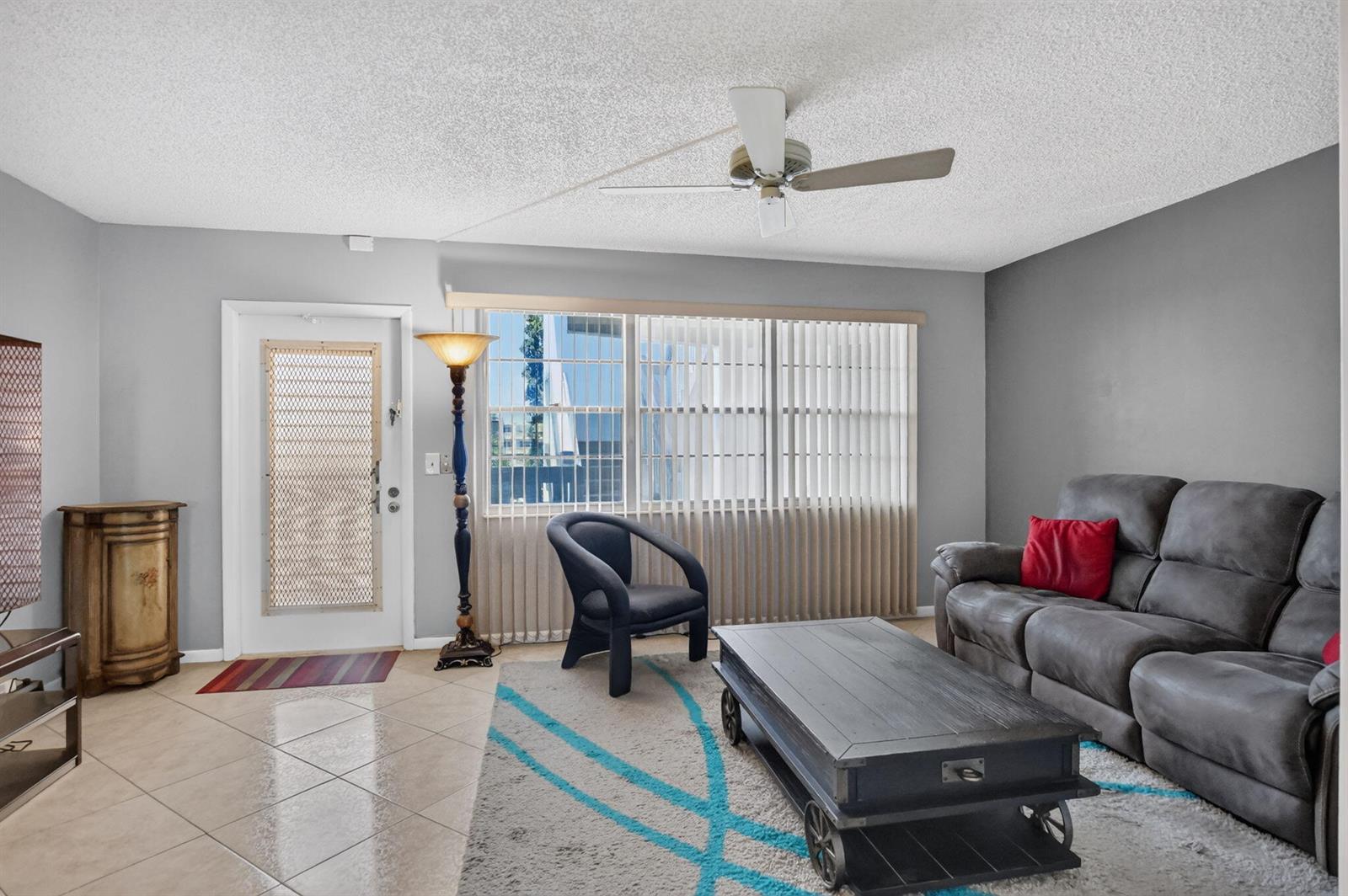 A living room features gray walls, tile flooring, a gray sofa, a coffee table, and a ceiling fan — 3090 Wolverton E, Boca Raton FL 33434, BOCA RATON, FL
