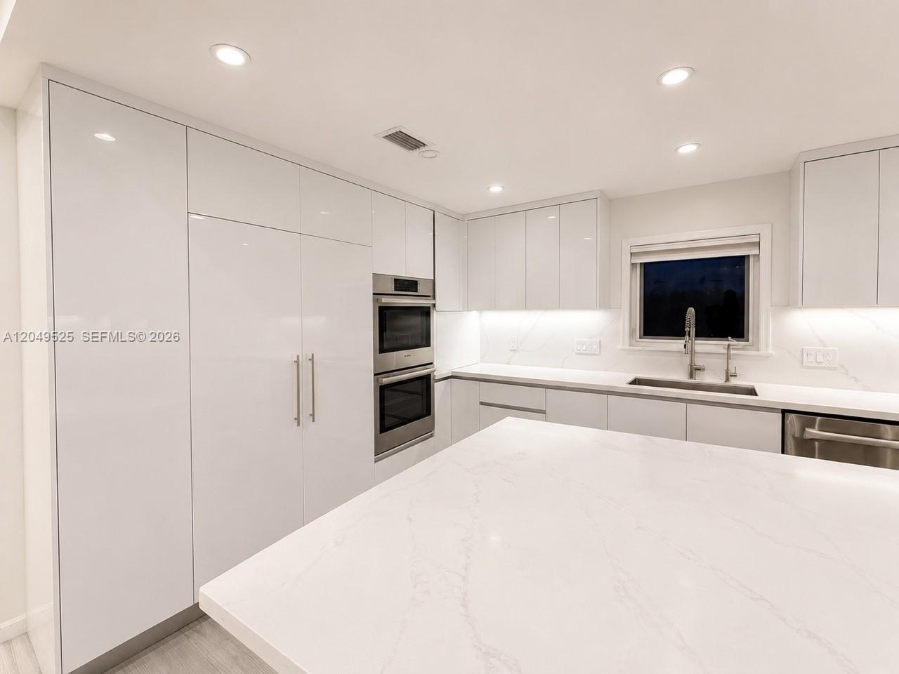 A modern kitchen features white glossy cabinetry, a marble-patterned island, and stainless steel appliances — 2616 Oakbrook Ct, Weston FL 33332, WESTON, FL