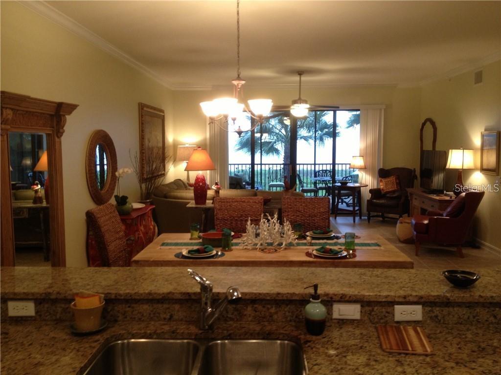A kitchen sink overlooks a dining area and living room with a view of palm trees — 89 VIVANTE BOULEVARD UNIT 203, PUNTA GORDA, FL