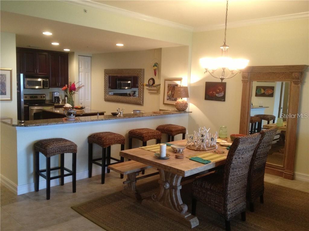 A dining area with a wooden table and wicker chairs sits before a kitchen counter — 89 VIVANTE BOULEVARD UNIT 203, PUNTA GORDA, FL