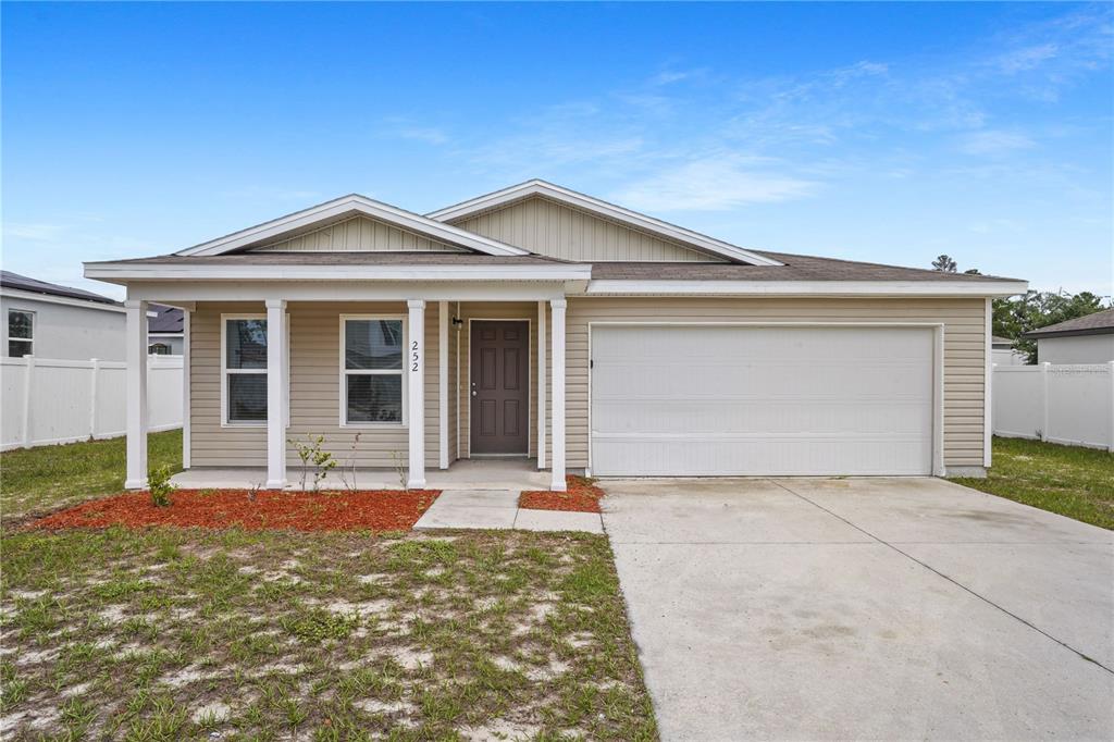 A single-story house with beige vinyl siding, a two-car garage, and a covered front porch — 252 FIG COURT, KISSIMMEE, FL