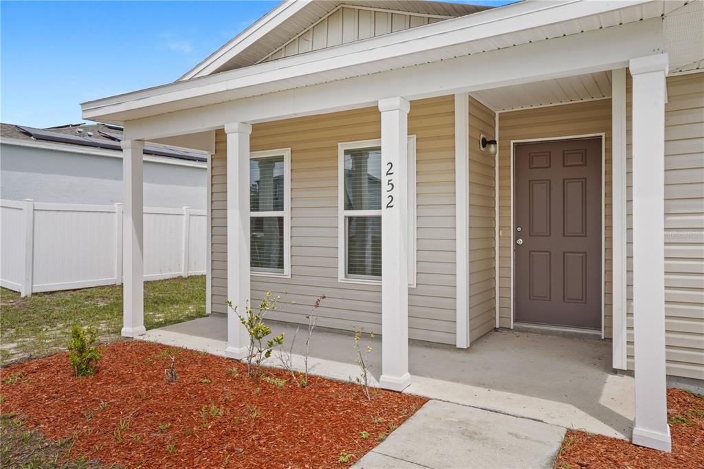 A tan-sided house exterior features a covered front porch with white columns and mulch — 252 FIG COURT, KISSIMMEE, FL