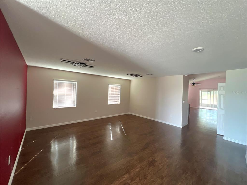 An empty living room features dark wood-look flooring, light walls, and a red accent wall — 205 BELLA VERANO WAY, DAVENPORT, FL